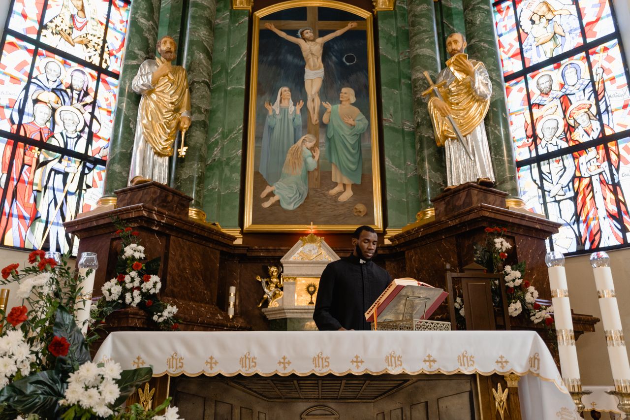 Priest delivering a sermon at an elaborate altar in a Catholic church with stained glass windows.