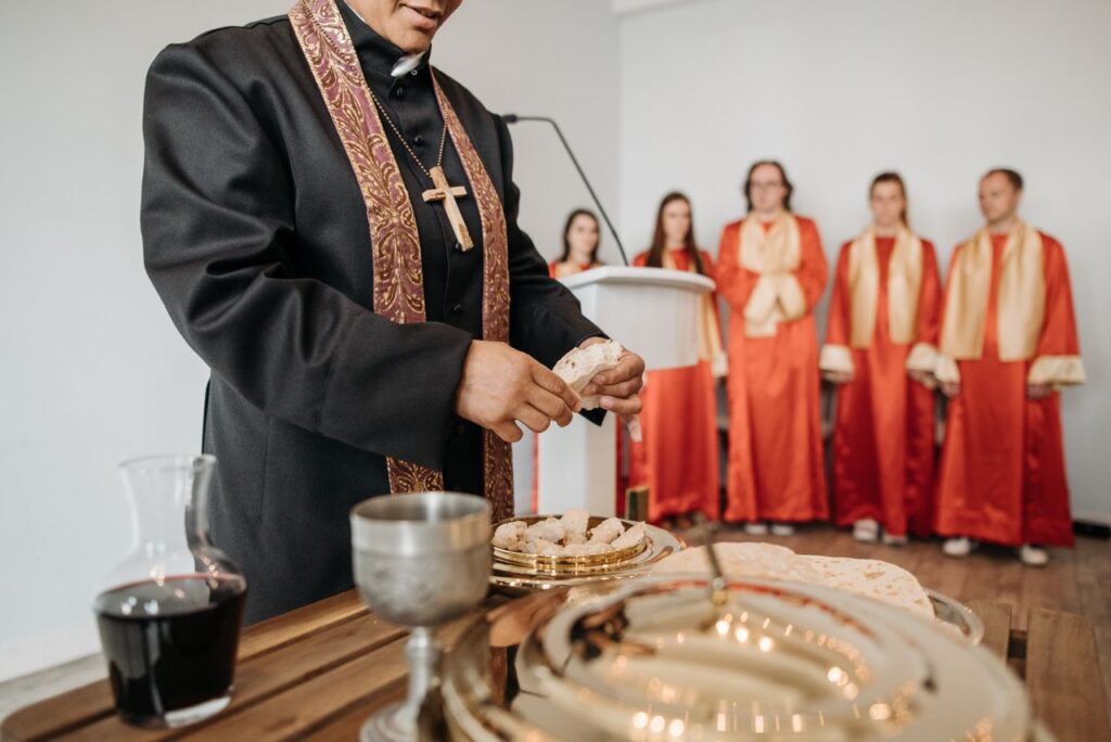 A pastor conducts communion during a church service with a choir in the background.